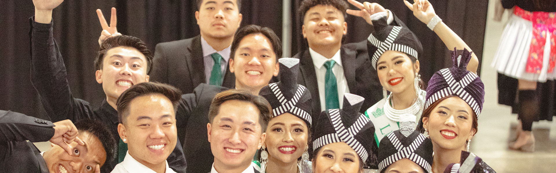 A group of young men and women posing for a photo in traditional hmong dresses and suits.