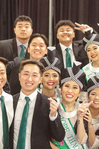 A group of young men and women posing for a photo in traditional hmong dresses and suits.